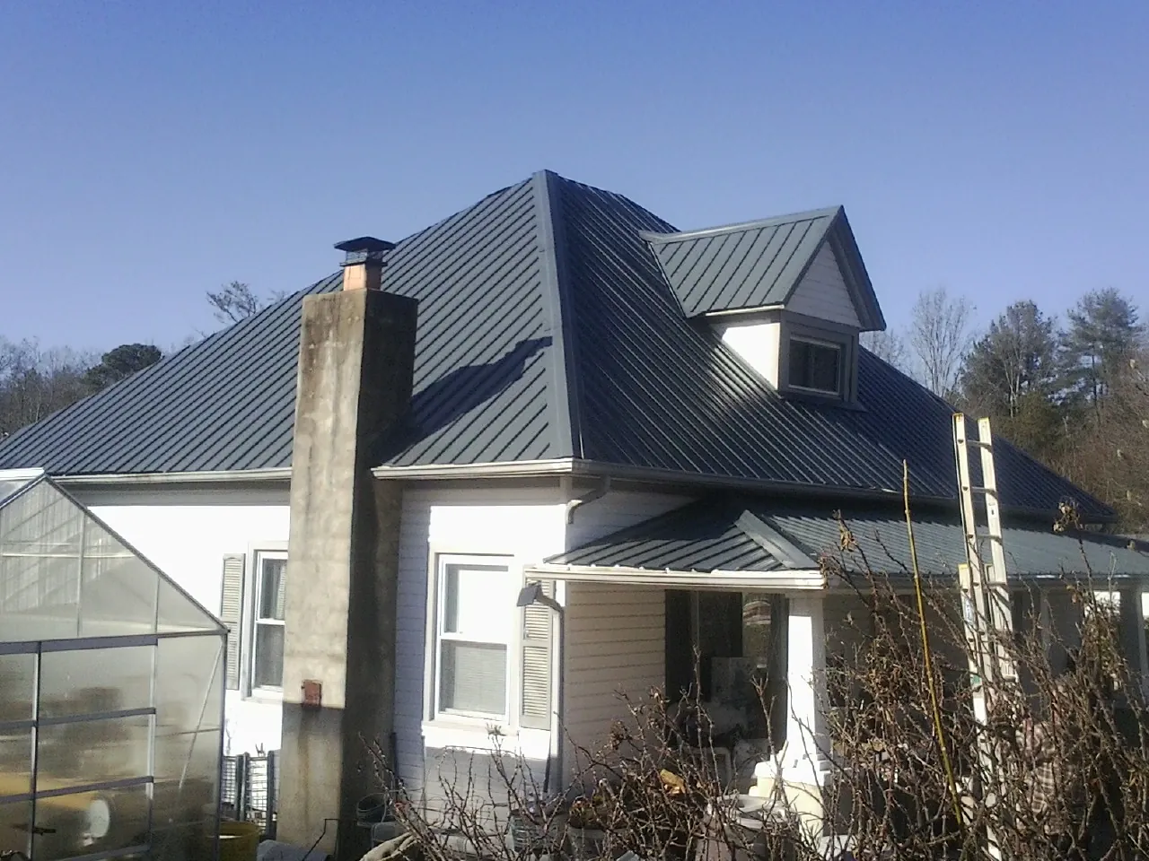 Dark blue standing seam metal roof on a white farmhouse with dormer — Slate & Tile Roof Repair by Roofing Brothers in Staffordsville