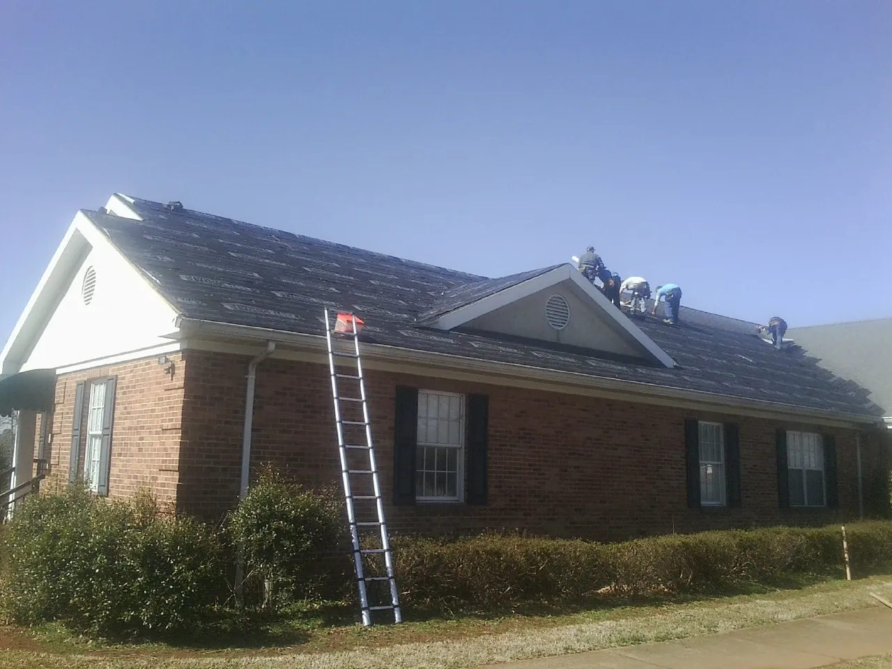 Crew tearing shingles off a brick ranch roof with a ladder set — Metal Roof Repair work by our crew in Staffordsville