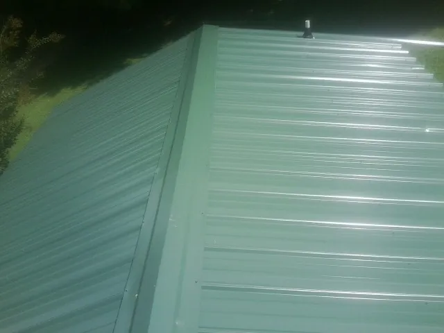 New green metal panels meeting at the ridge of a roof — Flat Roof Repair work by our crew in Staffordsville