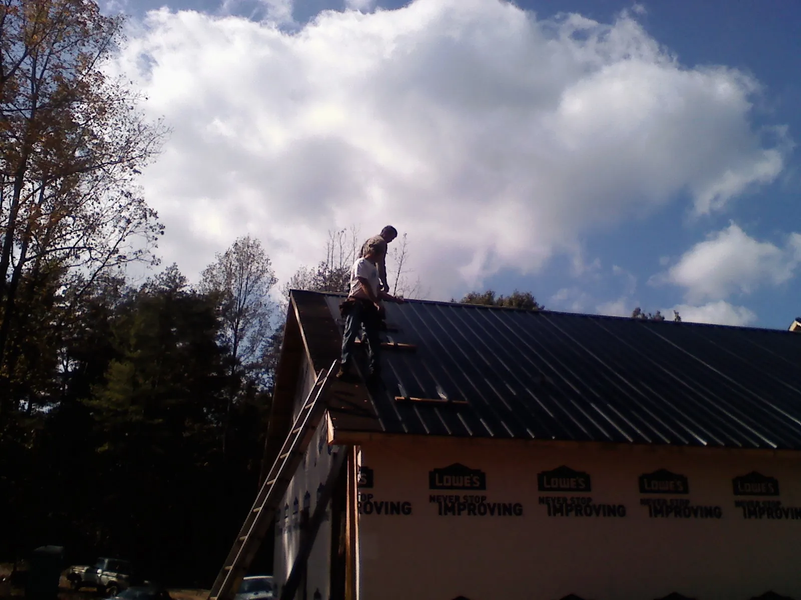 Roofer fastening dark metal panels high against a cloudy sky, from a Roof Inspection job in Staffordsville